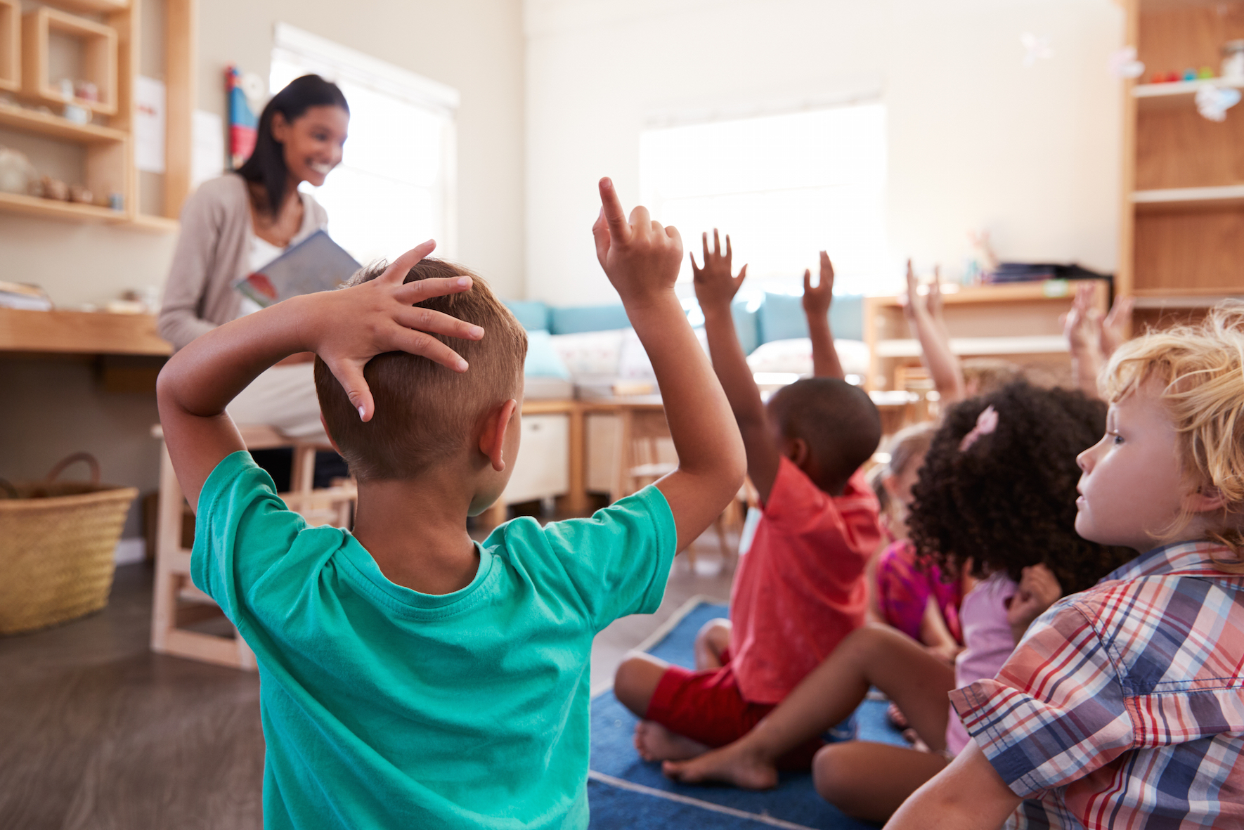 Primary school children in the classroom with their hands up as the teacher reads a story